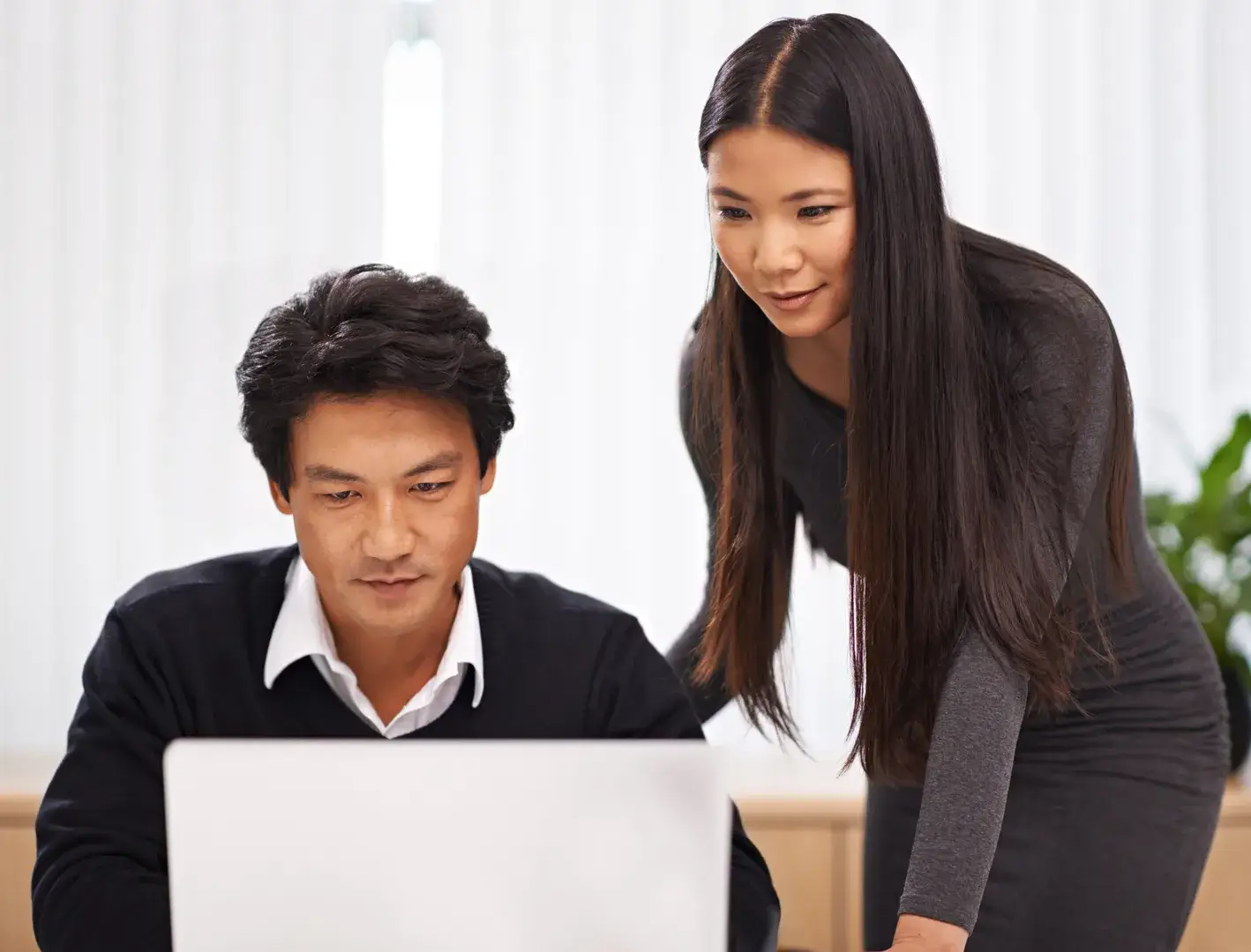 Woman mentoring an East Asian businessman at a laptop in a modern office